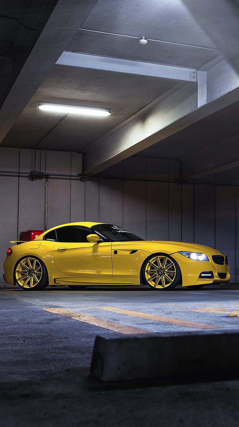 Yellow BMW Z4 sports car with gold rims and lowered suspension parked in a dark concrete industrial garage.