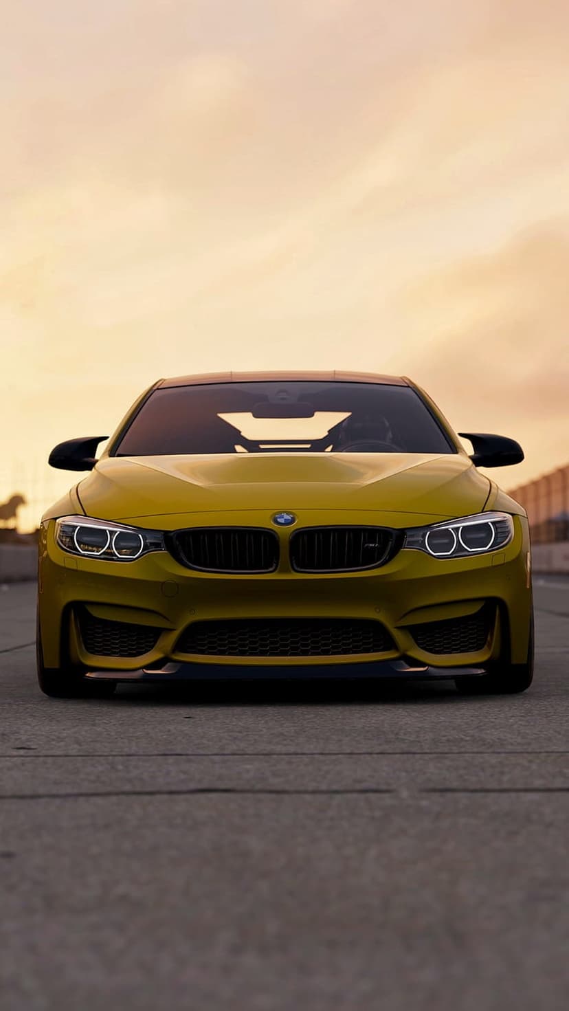 Yellow BMW M4 convertible parked on asphalt with warm sunset light hitting the front grille and headlights.
