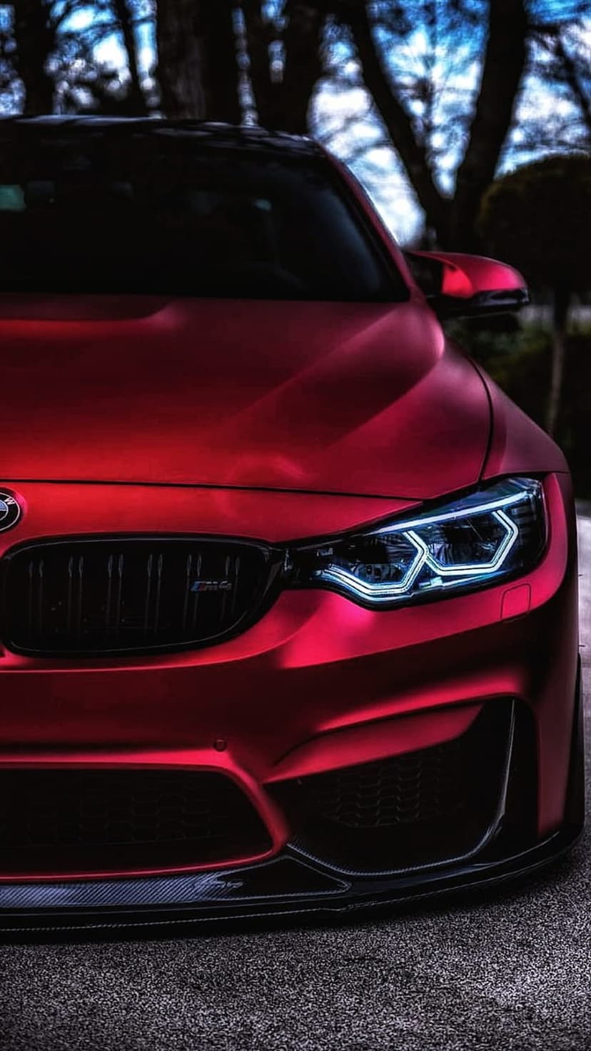 BMW M4 Coupe featuring hexagonal LED headlights and a carbon fiber splitter against a blurred tree background.