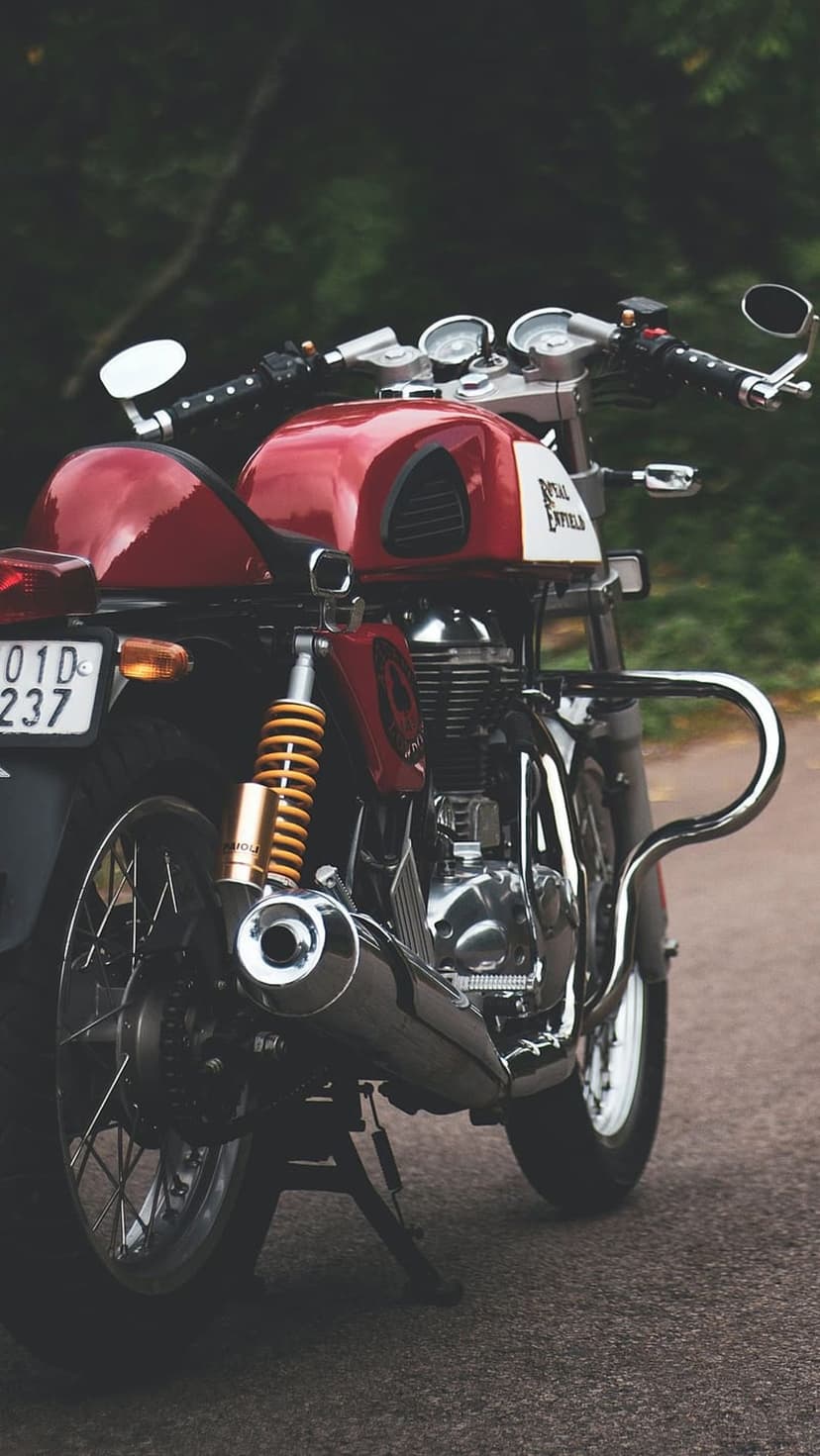 Red Royal Enfield motorcycle engine and fuel tank with chrome accents against a blurred green forest backdrop.