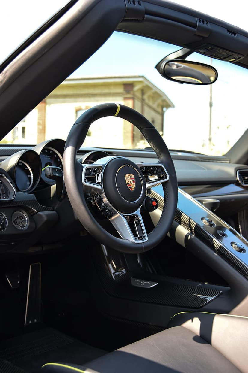 Porsche steering wheel with yellow stripe and gold crest in front of a digital car dashboard with carbon fiber.