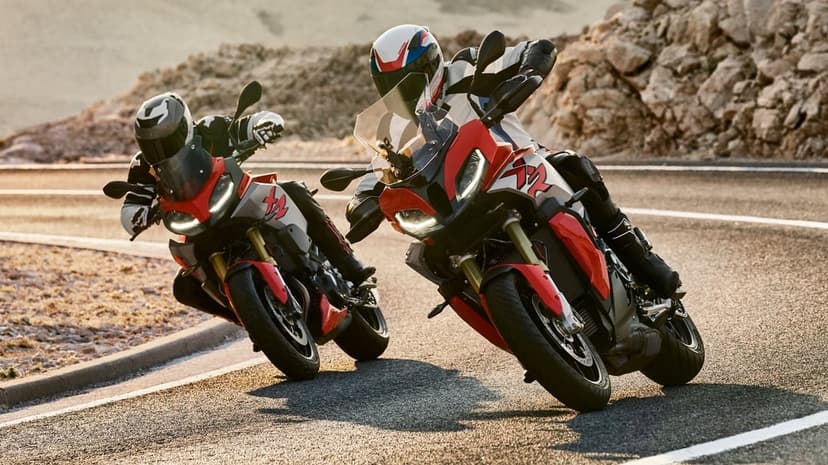 Two red and silver sport motorcycles leaning into a turn on a mountain highway during a warm golden hour sunset.