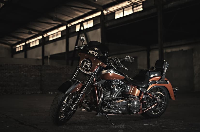 Orange Harley Davidson motorcycle with chrome accents parked inside a dark, sunlit industrial warehouse.