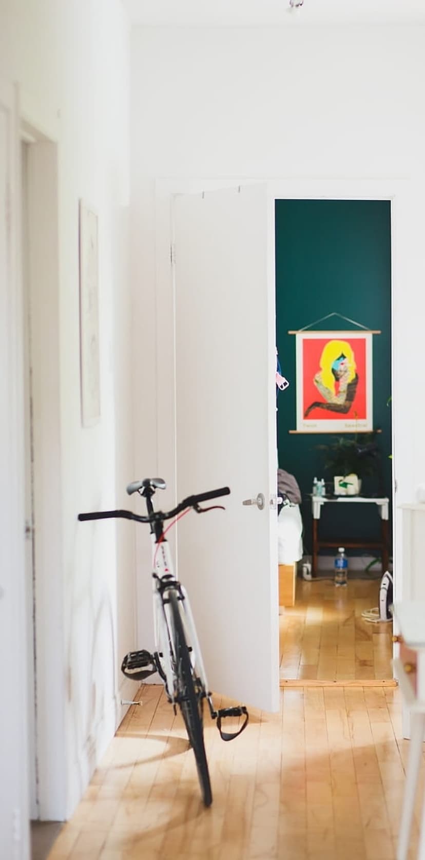 Bicycle leaning against a white hallway wall next to a doorway showing a red portrait on dark green walls.