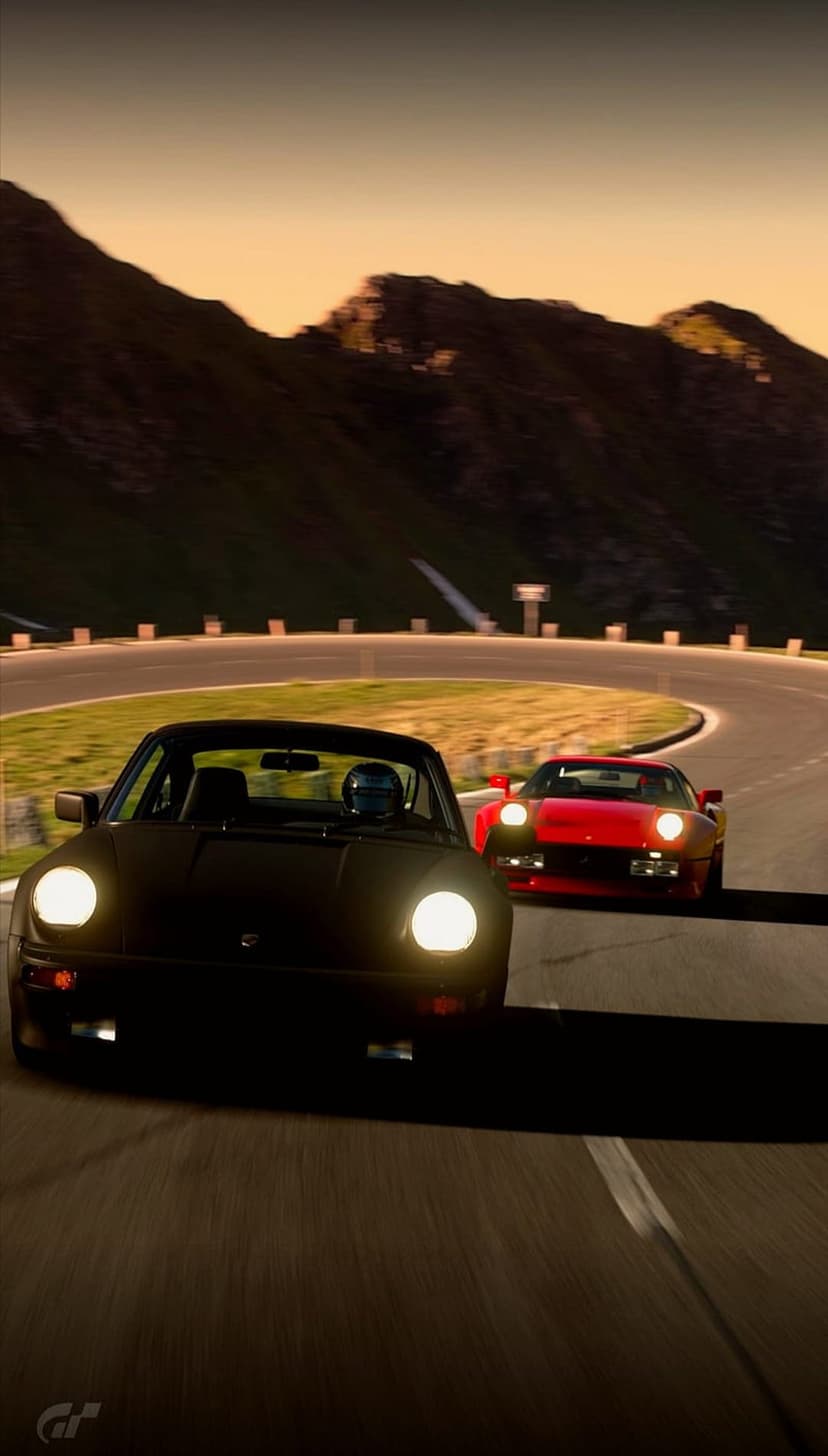 Black Porsche and red Ferrari navigate a winding mountain road during a vibrant golden hour alpine sunset.