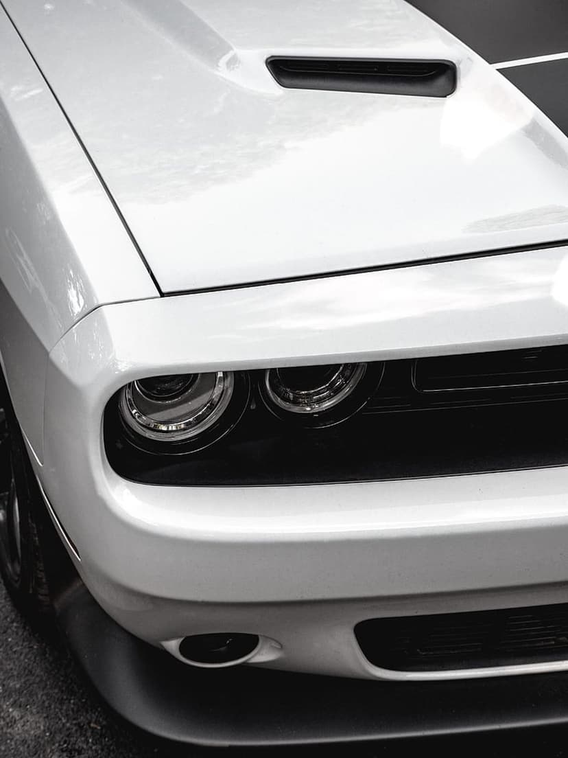 White Dodge Challenger front-end features black racing stripes, projector headlights, and a low chin spoiler.