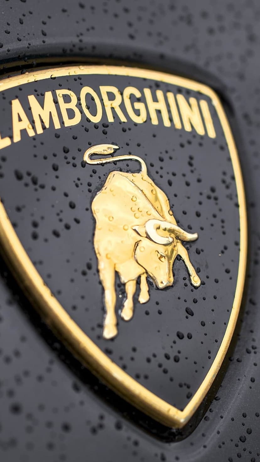 Gold Lamborghini shield emblem featuring a charging bull and raindrops on a dark metallic surface.