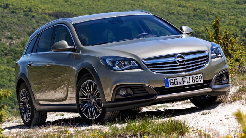 Metallic green Opel Insignia Country Tourer SUV on a dirt track against a blurred green hillside backdrop.
