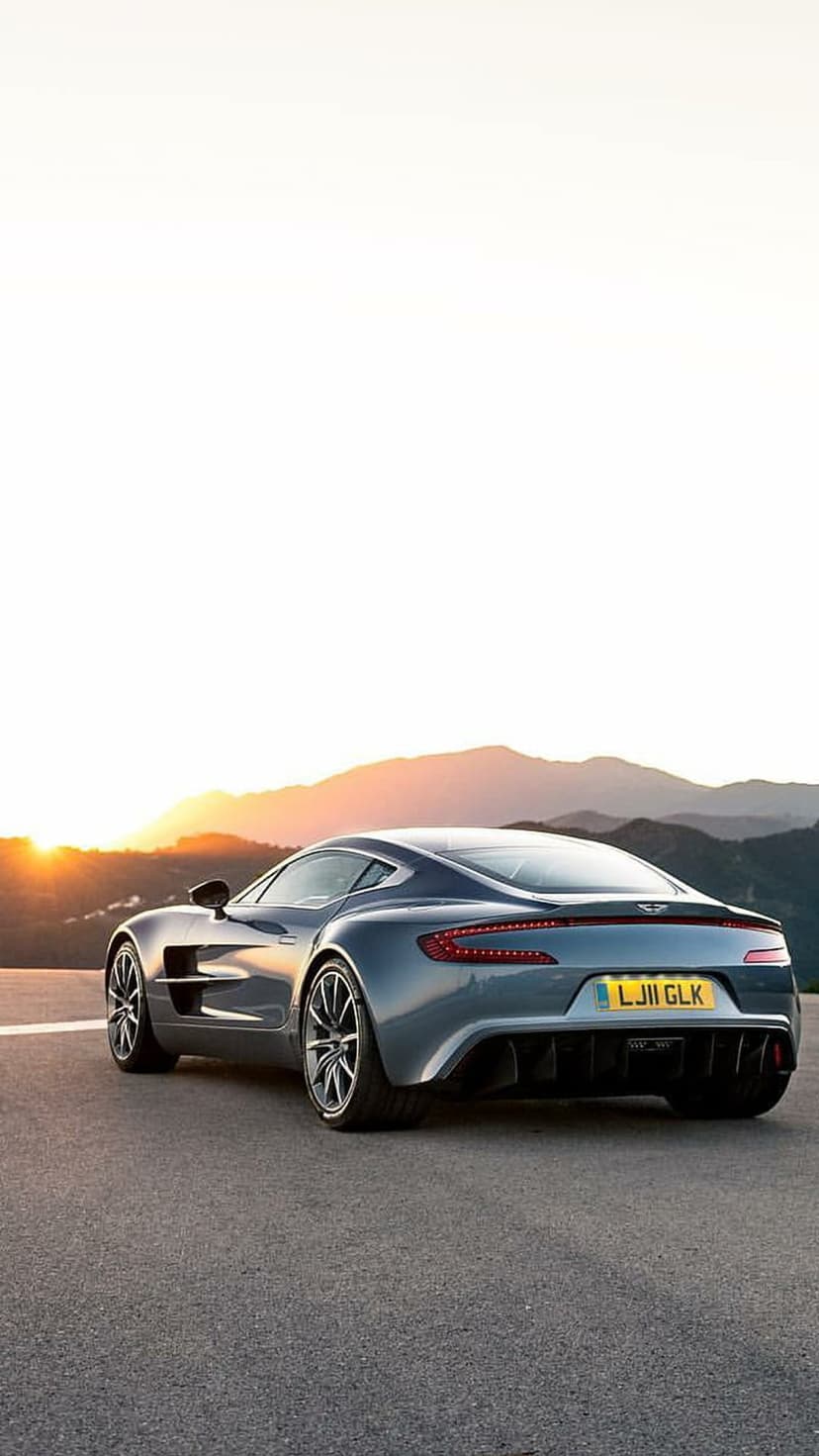 Aston Martin One-77 rear view with glowing LED taillights on a mountain road at golden hour during sunset.