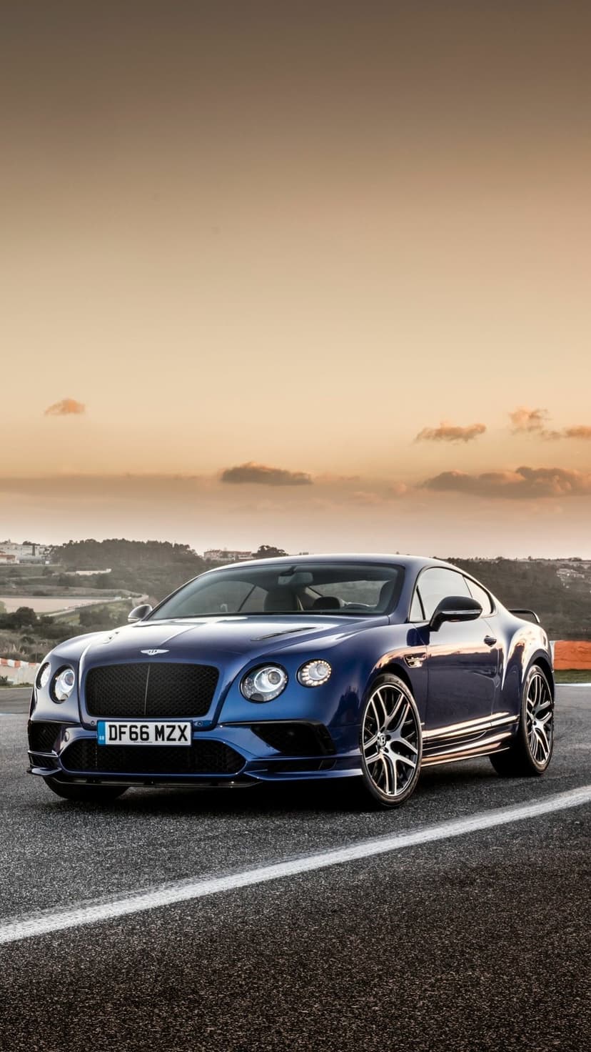 Front view of a dark blue luxury coupe on a paved road under a golden sunset sky with soft clouds.