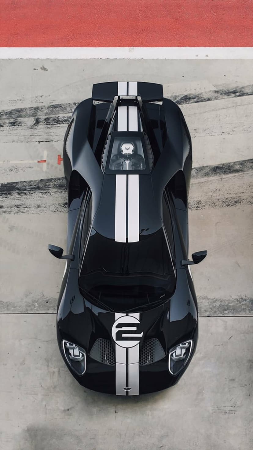Black Ford GT race car with white stripes captured from above on a concrete track with red and white borders.