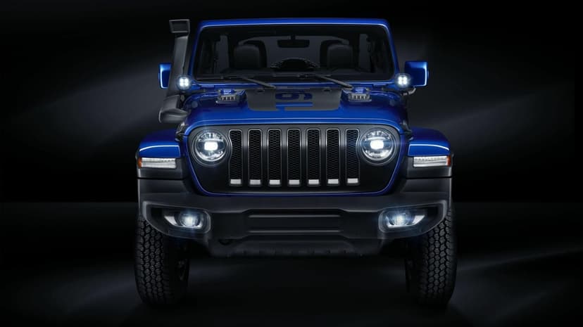 Front profile of a blue Jeep Wrangler with bright LED headlights and off-road gear against a dark background.