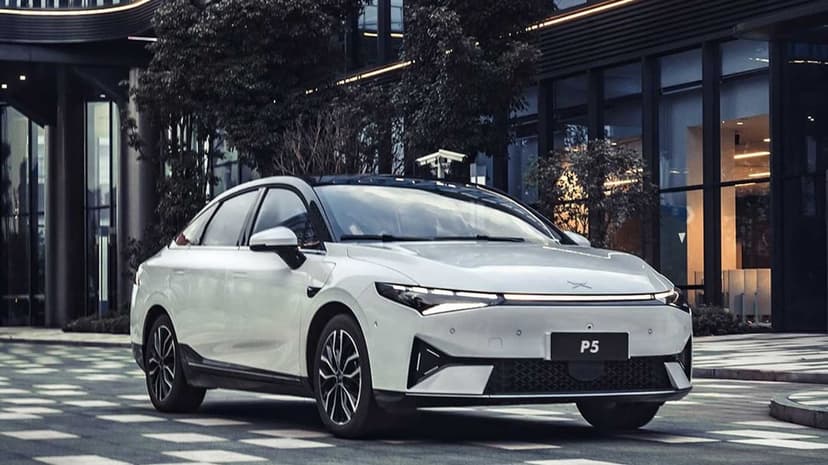 White electric sedan parked on patterned city pavement in front of a modern glass office building at dusk.