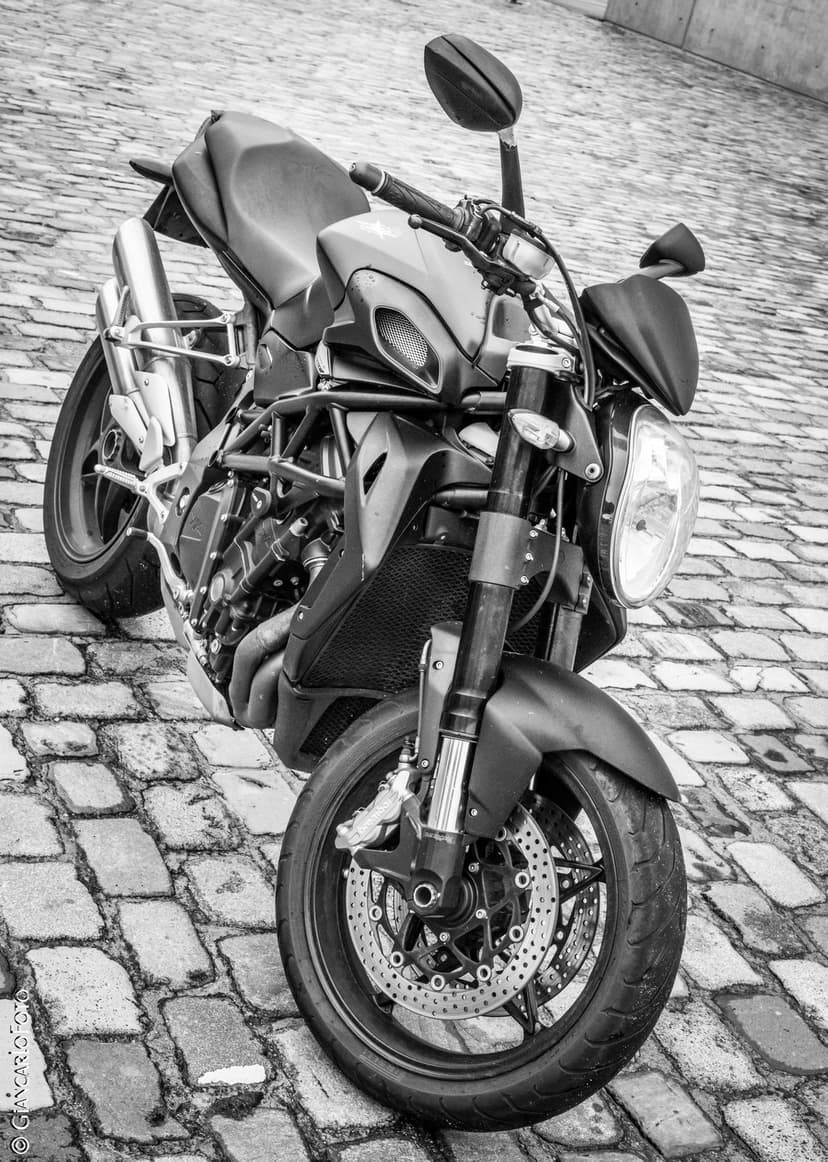 Modern motorcycle parked on an uneven cobblestone street featuring high-contrast black and white photography.