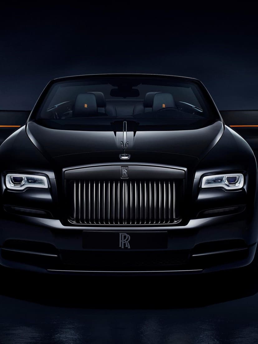 Front view of a black Rolls-Royce with a chrome grille, glowing headlights, and orange headrest embroidery.
