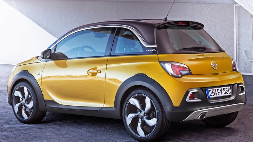 Yellow Opel Adam Rocks hatchback with a black roof and silver wheels against a minimalist grey wall background.