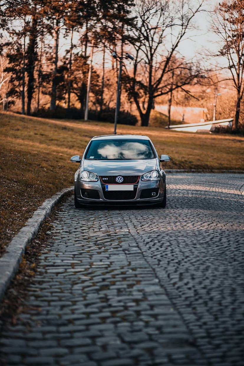 Gray Volkswagen GTI parked on a cobblestone road surrounded by orange autumn trees during a golden hour sunset.