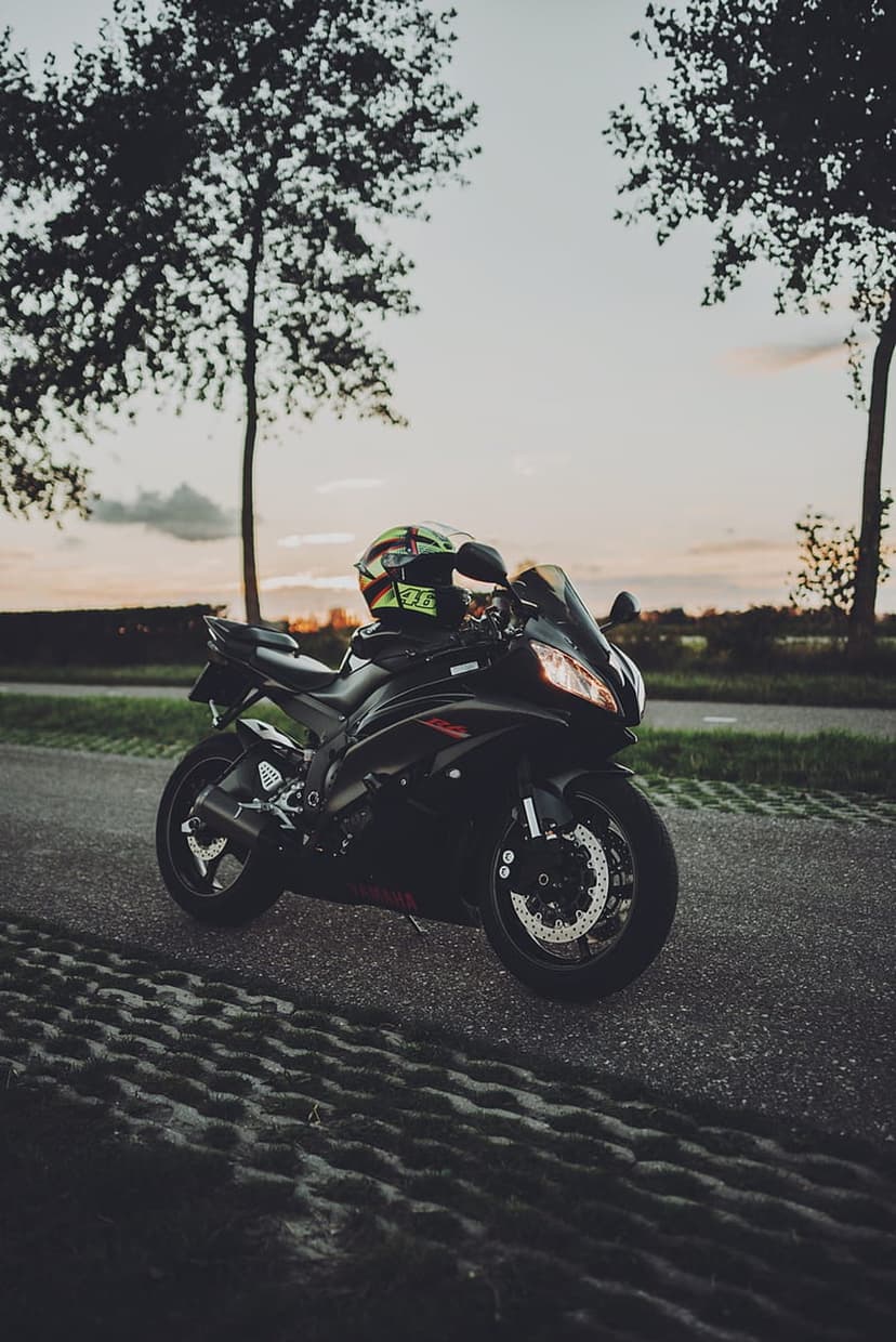 Black sport motorcycle and a colorful helmet parked on a road at sunset with silhouetted trees in the distance.