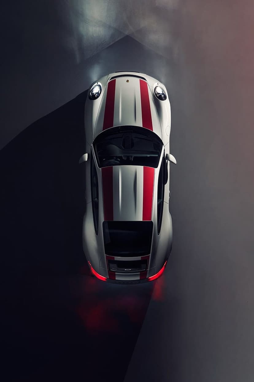 Silver sports car with red racing stripes parked on a dark reflective surface with glowing headlights.
