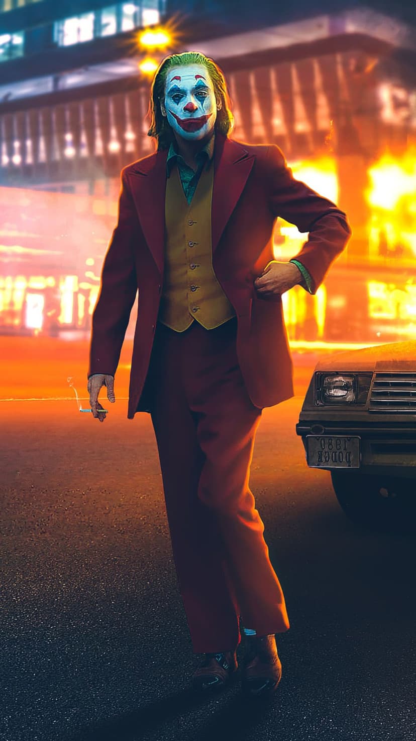 Joker in a red suit walks across a city street at night with glowing urban lights in the background.