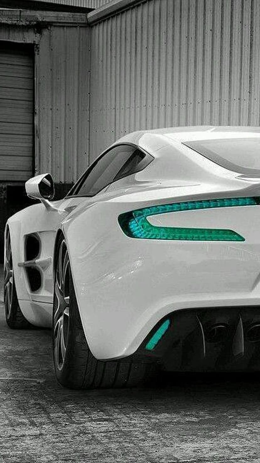 White sports car rear showing illuminated teal LED taillights against a textured industrial metal wall.