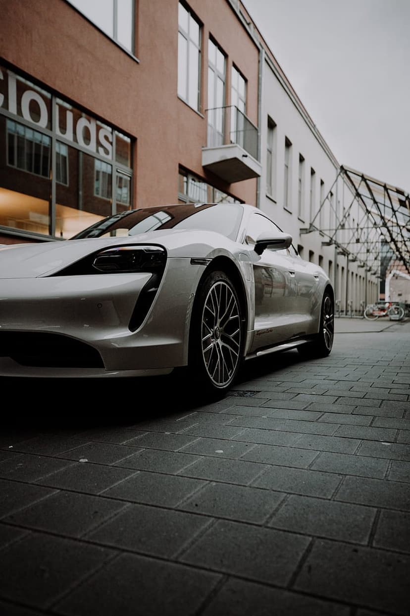 White luxury electric car parked on a textured cobblestone street by a glass building during golden hour.