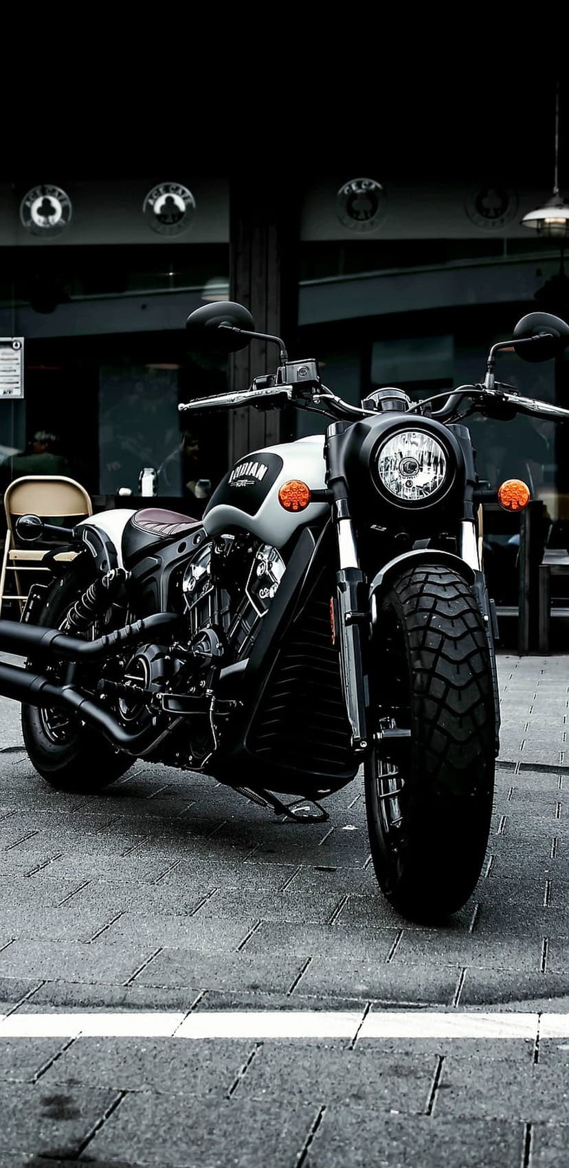 Indian Scout motorcycle with black bodywork and round headlight parked on a grey cobblestone urban street.