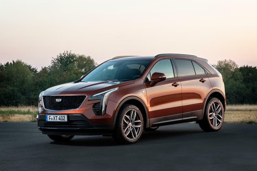 Metallic bronze Cadillac XT4 luxury SUV parked on asphalt at dusk with green trees in the soft-focus background.