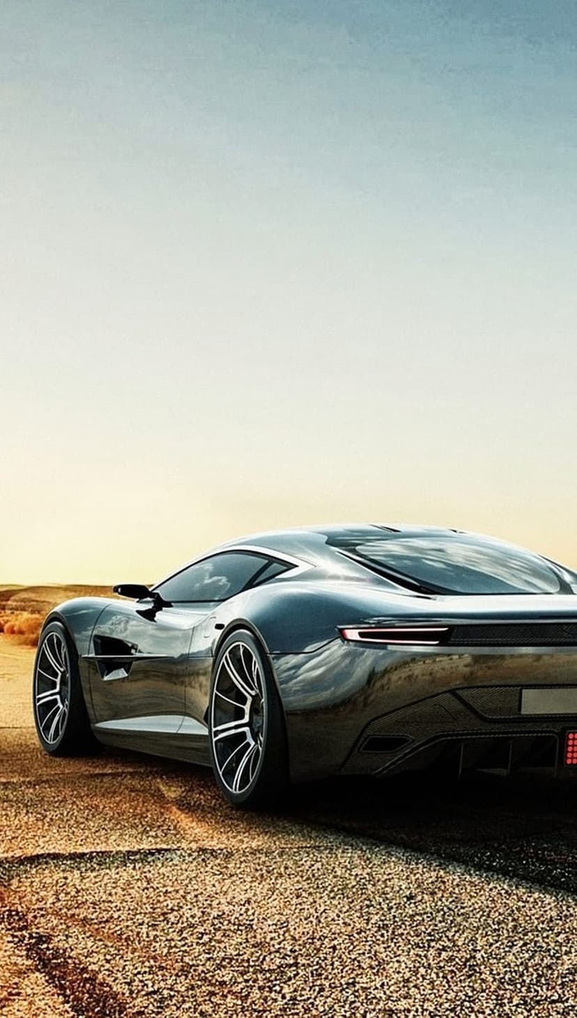 Black sports car on a gravel desert road at sunset with a glossy finish reflecting the warm orange sky.