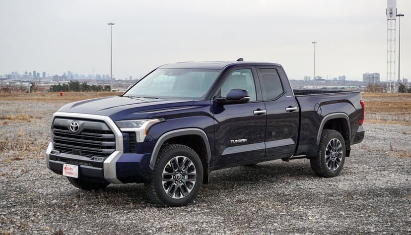 Dark blue Toyota Tundra truck parked on a gravel lot with a city skyline under a soft overcast sky.
