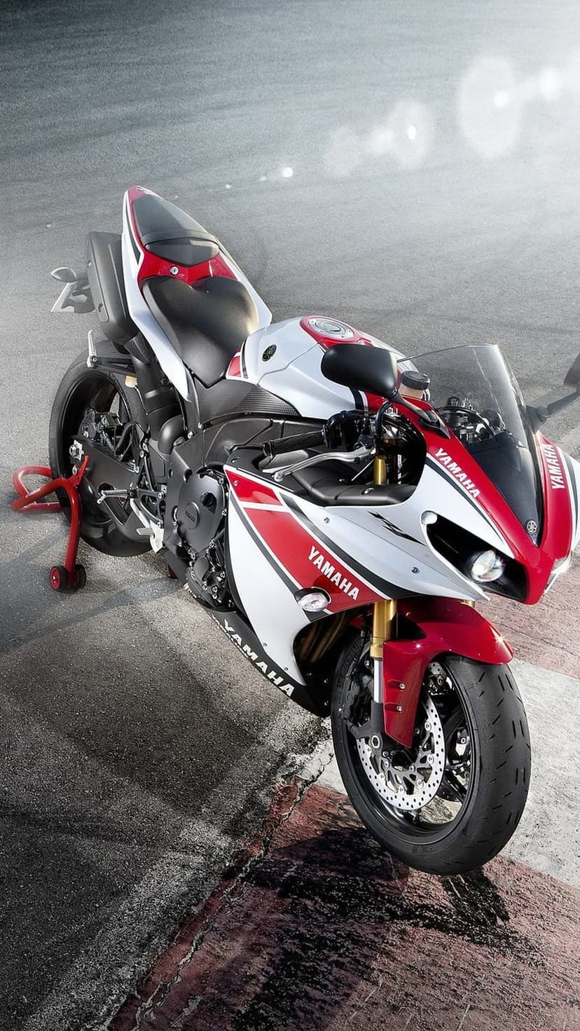 Red and white Yamaha sport motorcycle on a paddock stand atop a grey asphalt racetrack under bright daylight.