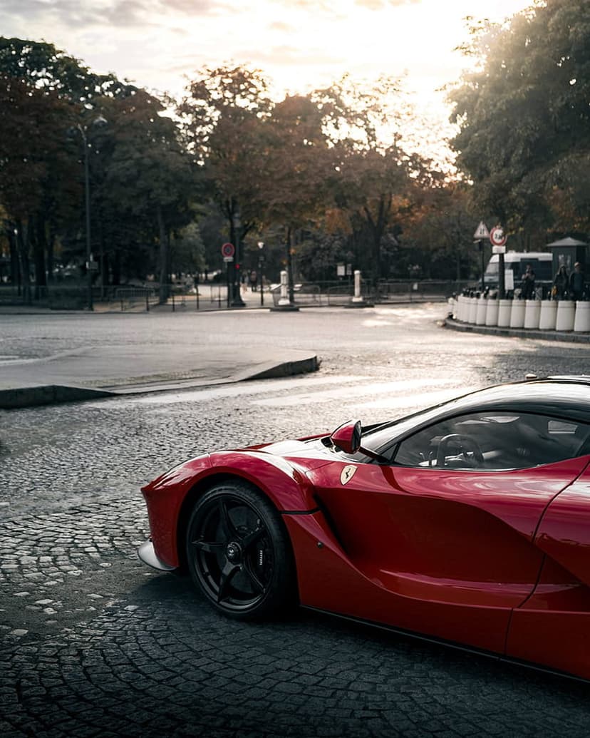 Red Ferrari supercar with black accents parked on a cobblestone street during a misty autumn day at low angle.