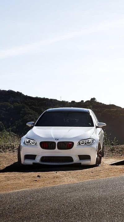 White BMW M5 parked on dusty road with hills background