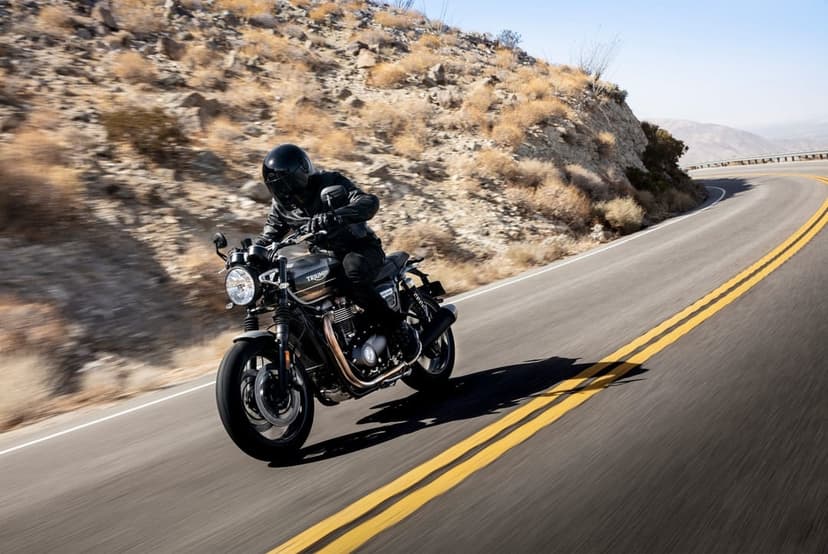 Motorcyclist on a black Triumph bike leans into a curve on a scenic desert mountain road under bright sunlight.