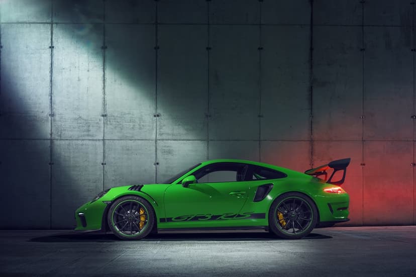 Green Porsche 911 GT3 RS side profile against a concrete wall with dramatic spotlight and red rear lighting.