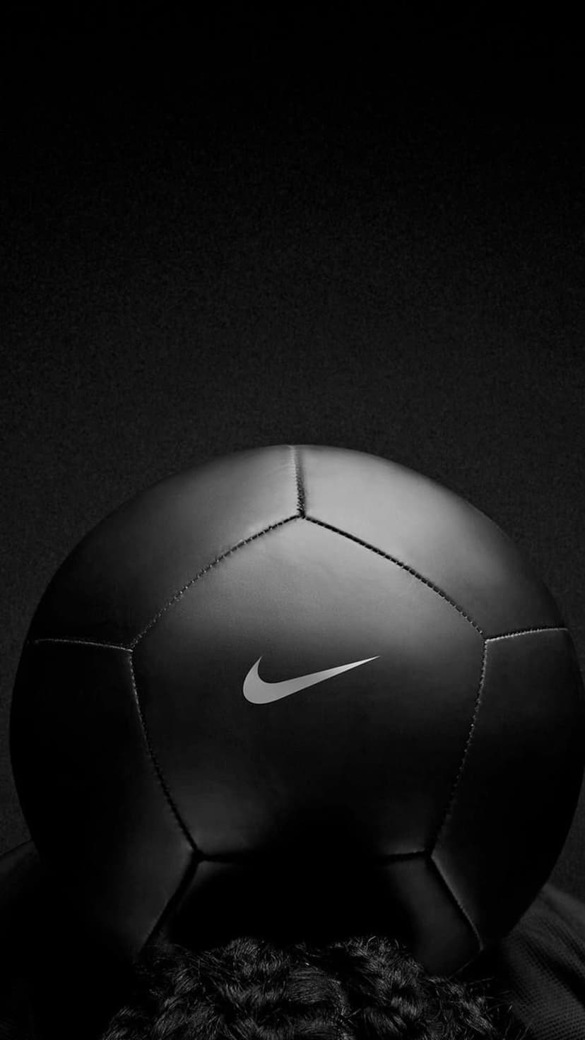 Black Nike soccer ball with a white swoosh logo featuring detailed stitching against a dark, shadowy background.