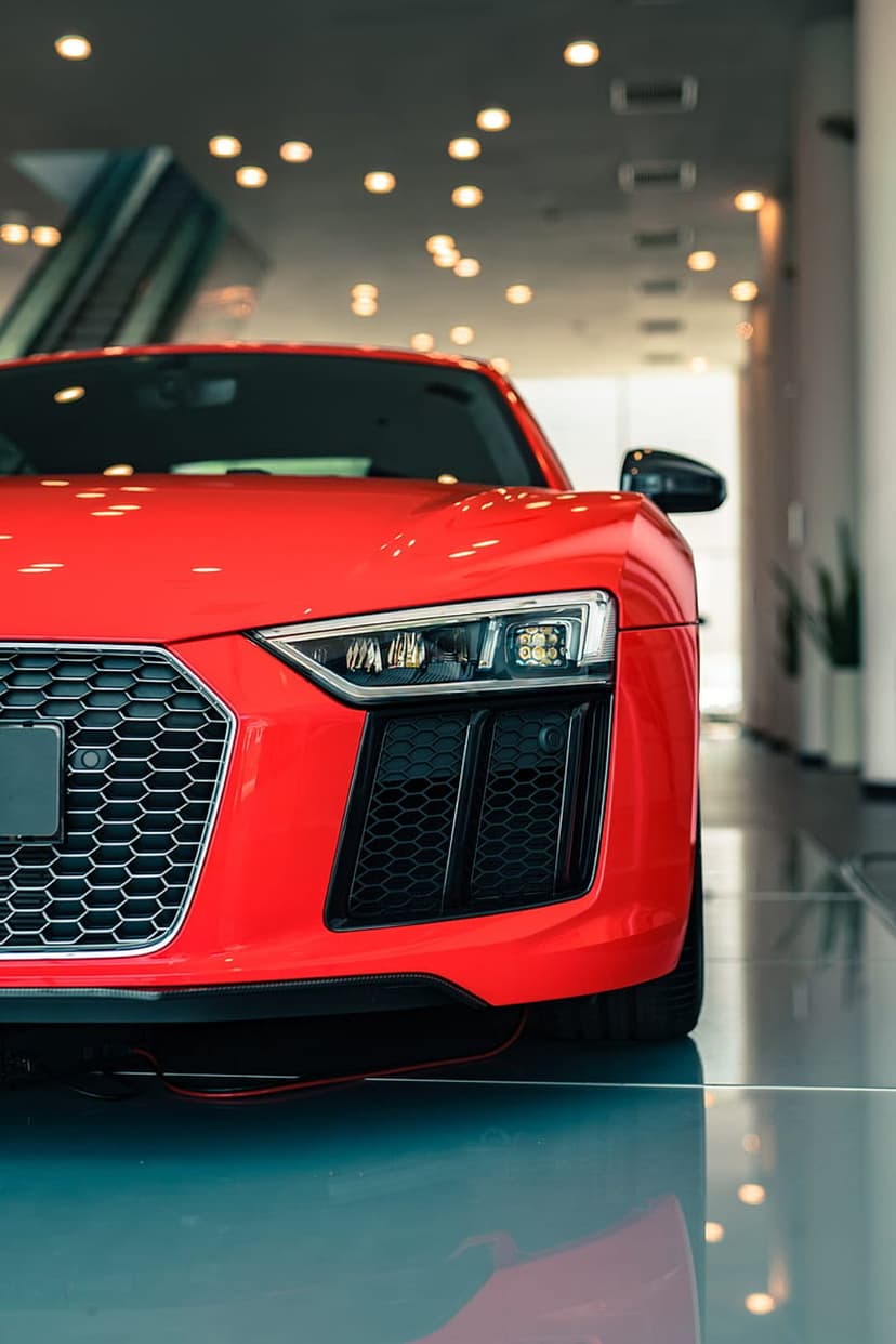 Red Audi R8 supercar with glowing LED headlights parked on a reflective showroom floor in a low-angle view.