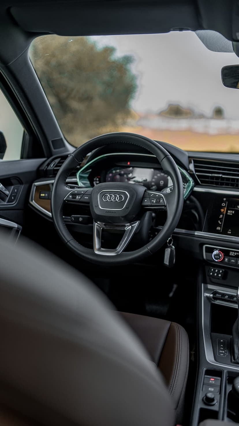 Audi Q3 steering wheel and digital dashboard next to a brown leather seat in a modern luxury SUV cabin.