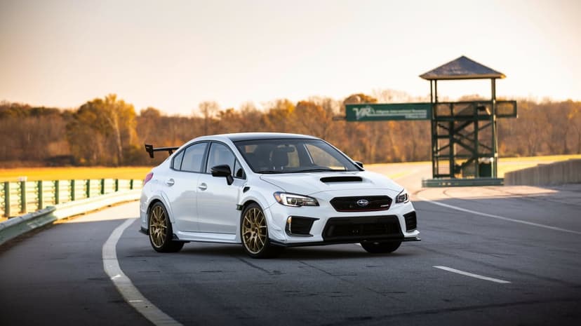 White Subaru WRX STI S209 with gold wheels on a racetrack curve during sunset with an observation tower.