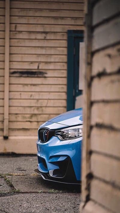 Blue BMW M4 Front View Mobile Wallpaper with Wood Backdrop