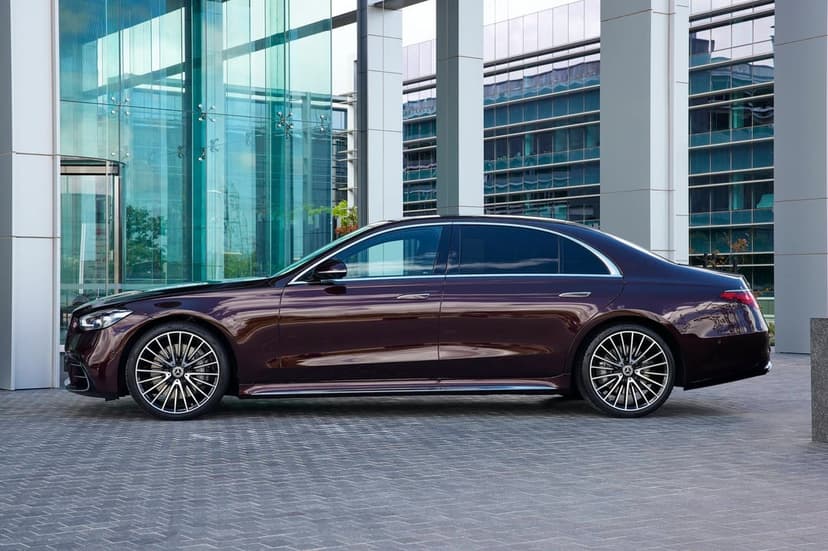 Dark red Mercedes-Benz sedan with silver multi-spoke wheels parked beside a modern glass architectural building.