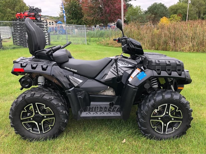 Black Polaris Sportsman XP 1000 Touring ATV with rugged off-road tires parked on a vibrant green grass field.