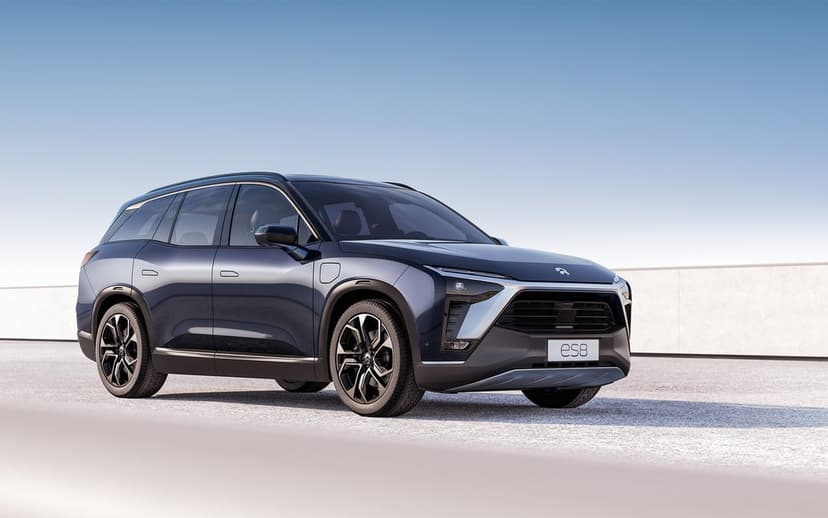 Blue NIO ES8 electric SUV parked on a paved surface against a clear sky and minimalist concrete wall.