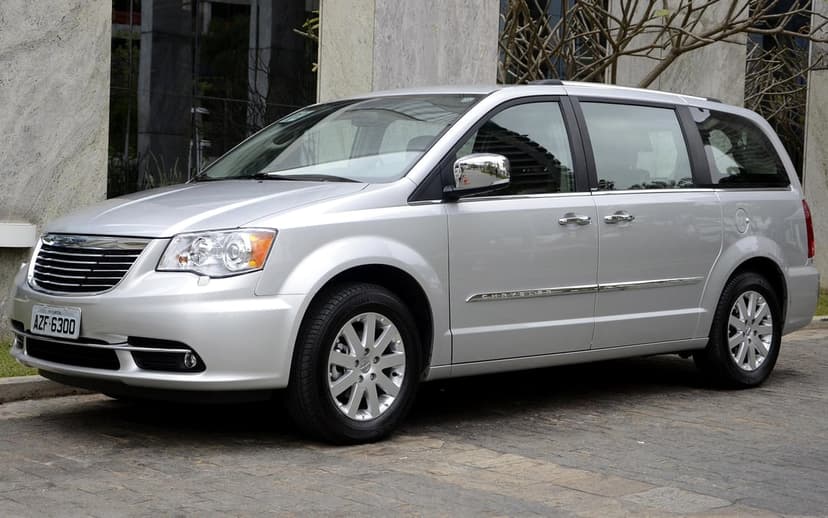 Silver Chrysler minivan parked on a paved driveway in front of a modern stone building under soft daylight.