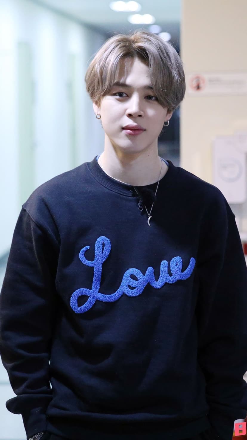 BTS member Jimin wearing a black sweatshirt with a blue Love graphic and a crescent moon necklace in a portrait.
