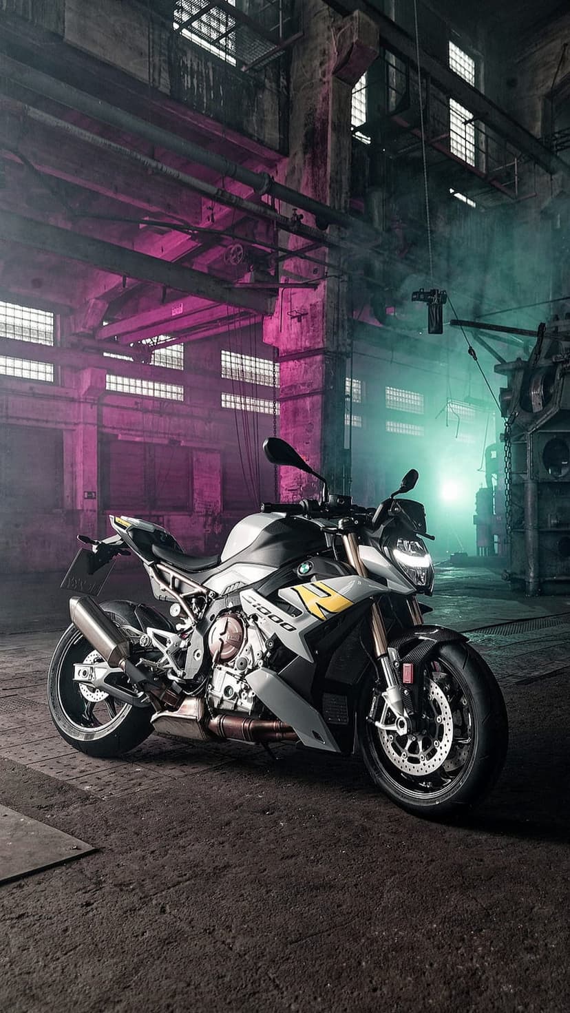BMW S1000R motorcycle parked in a smoky factory with pink and teal lighting reflecting on its black frame.