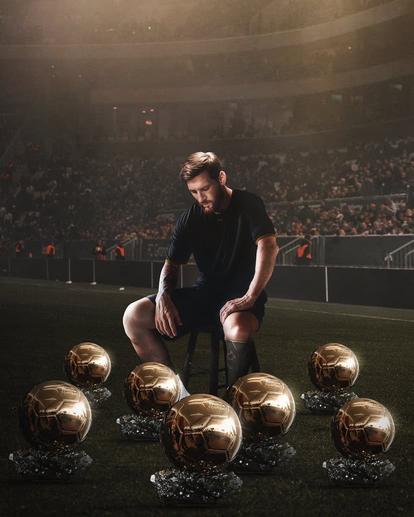Lionel Messi sits on a stool surrounded by various golden trophies on a dark, grass stadium field at night.