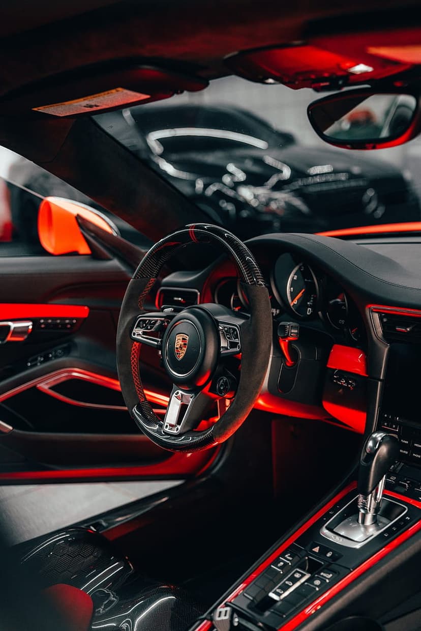 Porsche steering wheel and dashboard glowing with red ambient light for a high-end mobile phone backdrop.