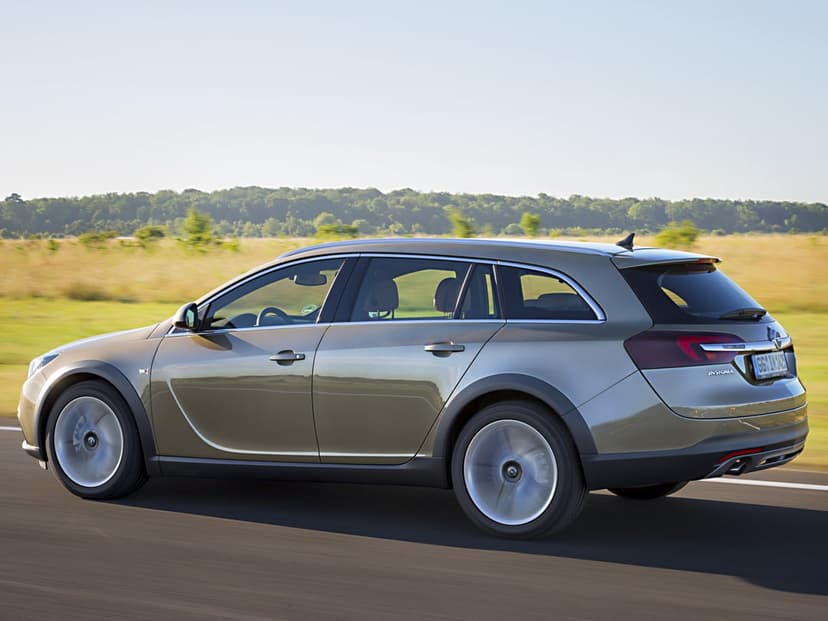 Bronze Opel Insignia station wagon driving fast on a sunlit road with green fields in the background.