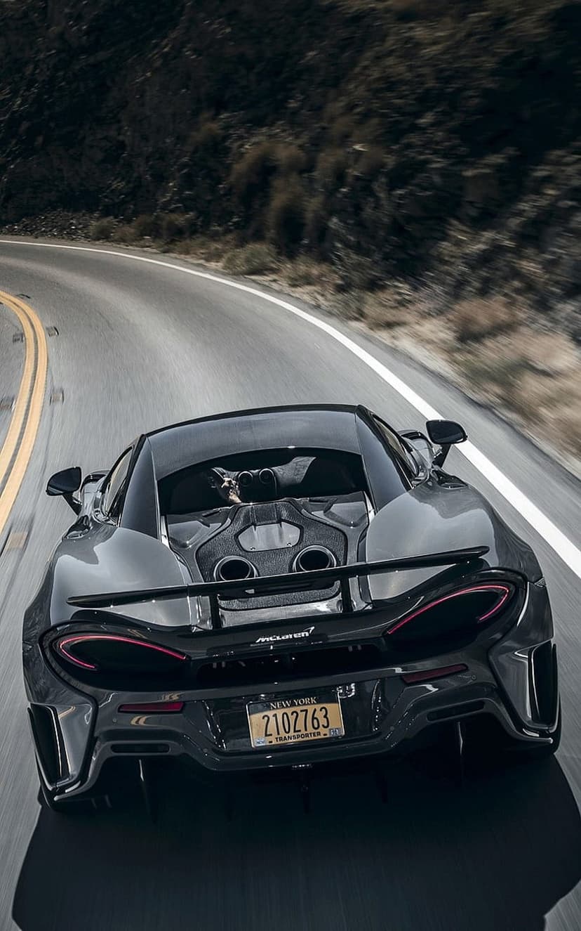 McLaren 570S rear exterior with glowing taillights speeding through a blurred mountain road during daytime.